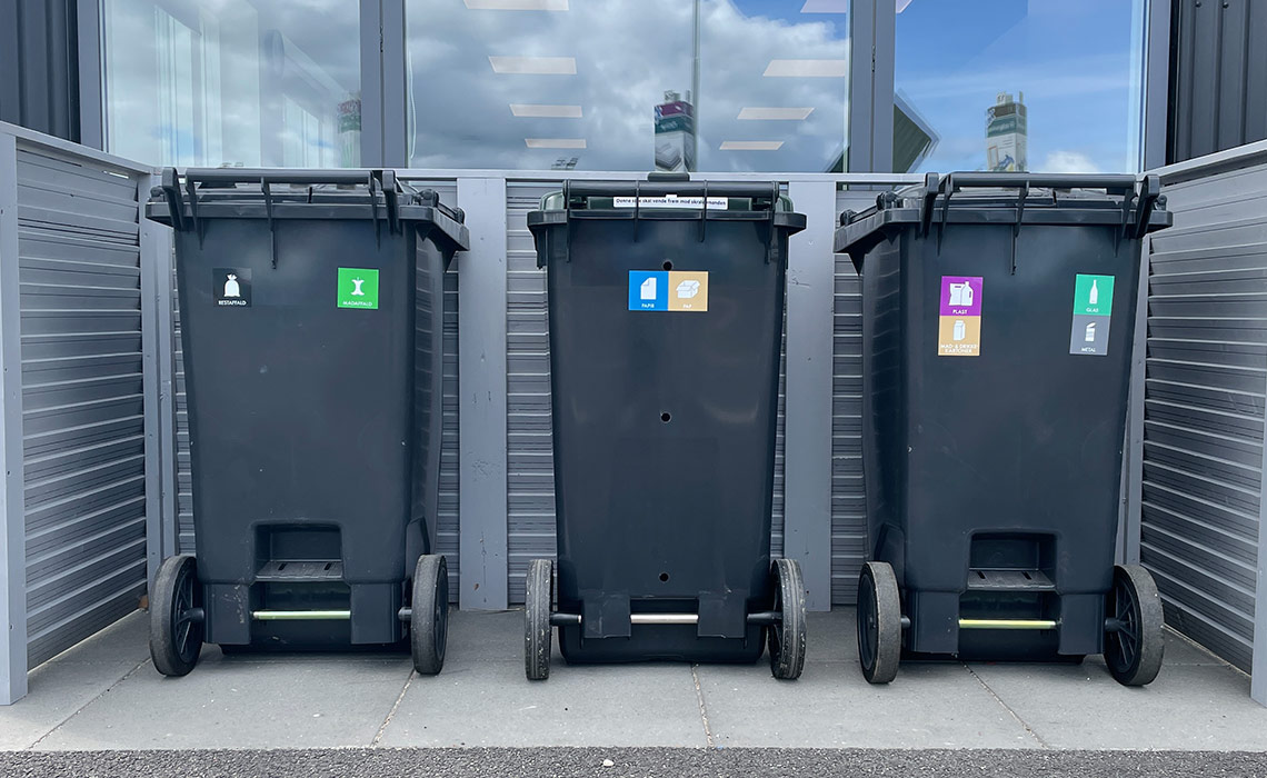 Tre beholdere til affaldssortering i udstilling på genbrugsplads